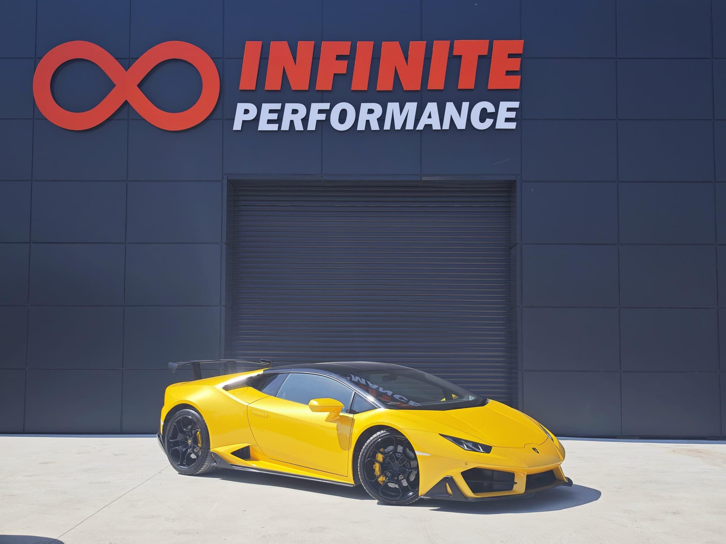 Atölye cephesi: Infinite Performance tabelası, kepenkli giriş ve önünde sarı bir spor otomobil