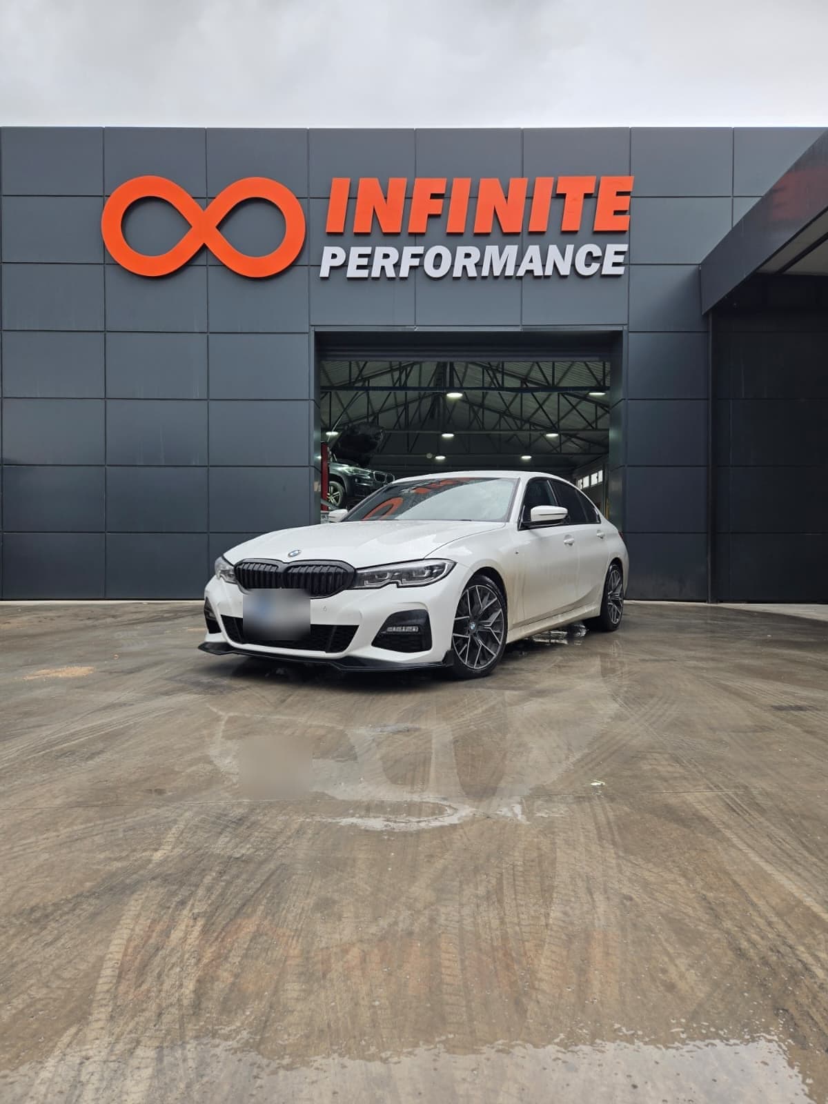 Atölye girişinin önünde beyaz bir BMW; üstte Infinite Performance tabelası