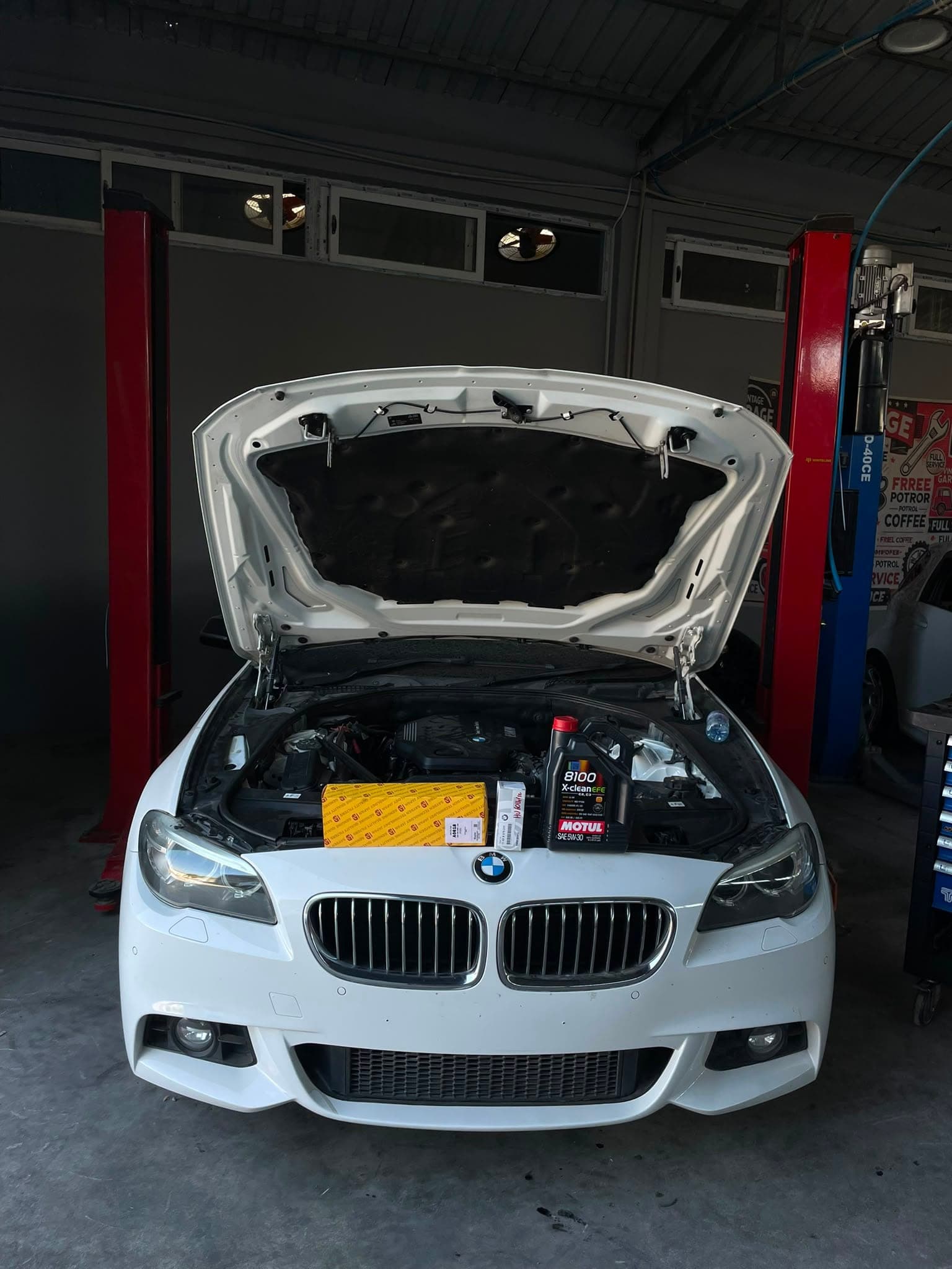 Kaputu açık beyaz bir BMW; motorun üzerinde motor yağı ve filtre kutusu