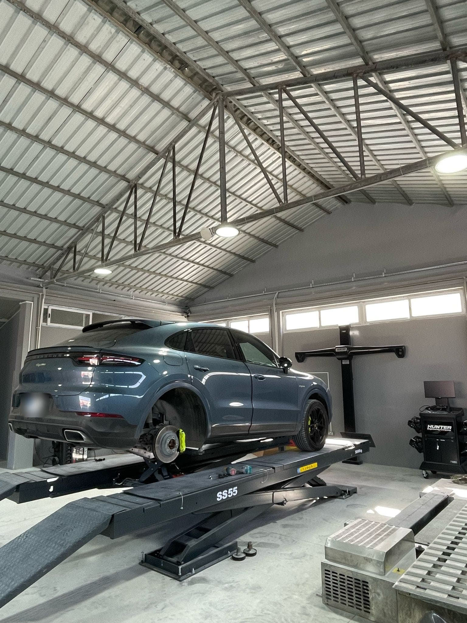 Makaslı liftte arka tekerleği sökülmüş gri bir Porsche; sağda Hunter rot ayar kamera kulesi ve konsolu