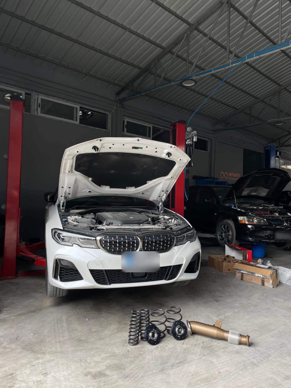 Kaputu açık beyaz bir BMW; zeminde bir downpipe ve süspansiyon yayları