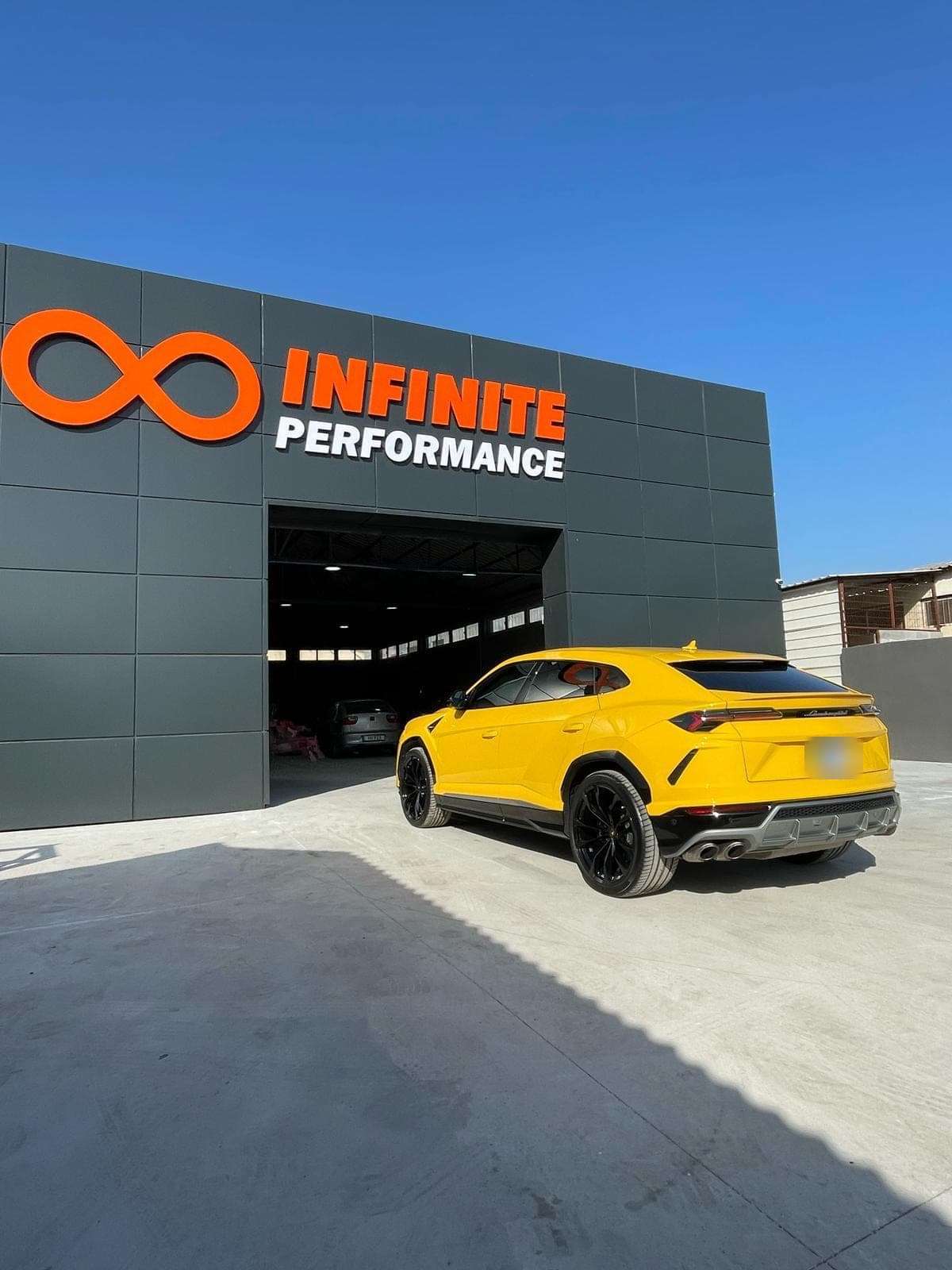 Atölye girişinin önünde sarı bir Lamborghini Urus; üstte Infinite Performance tabelası