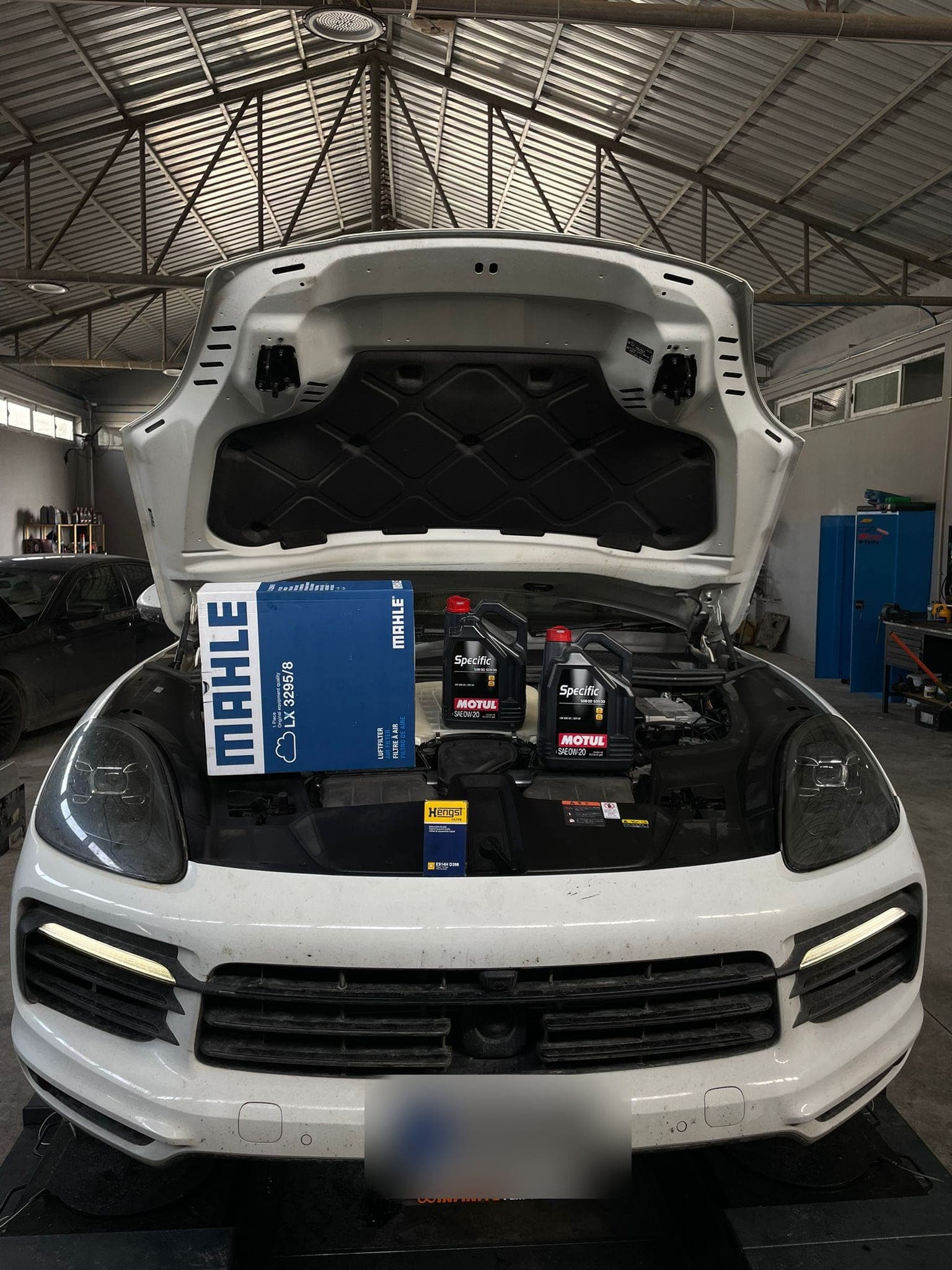 Kaputu açık beyaz bir SUV; motorun üzerinde motor yağı ve filtre kutuları