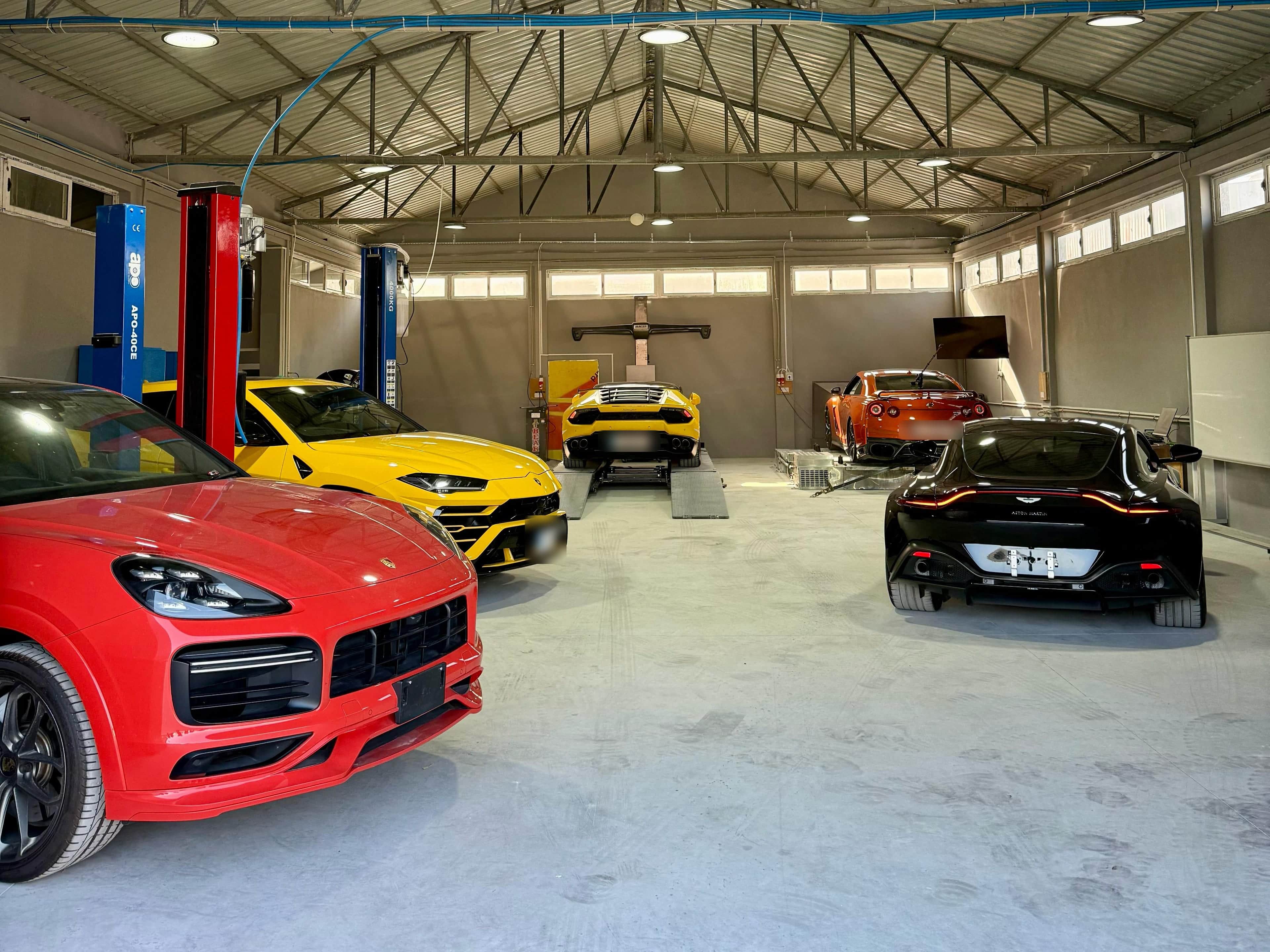 Atölyenin iç mekânı: önde kırmızı ve sarı iki SUV, arkada liftte sarı ve dinamometrede turuncu birer spor otomobil, sağda siyah bir spor otomobil